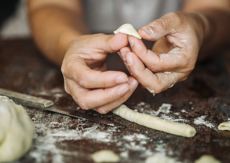 Hands crafting fresh orecchiette pasta from dough on a floured table during luxury Puglia tours.