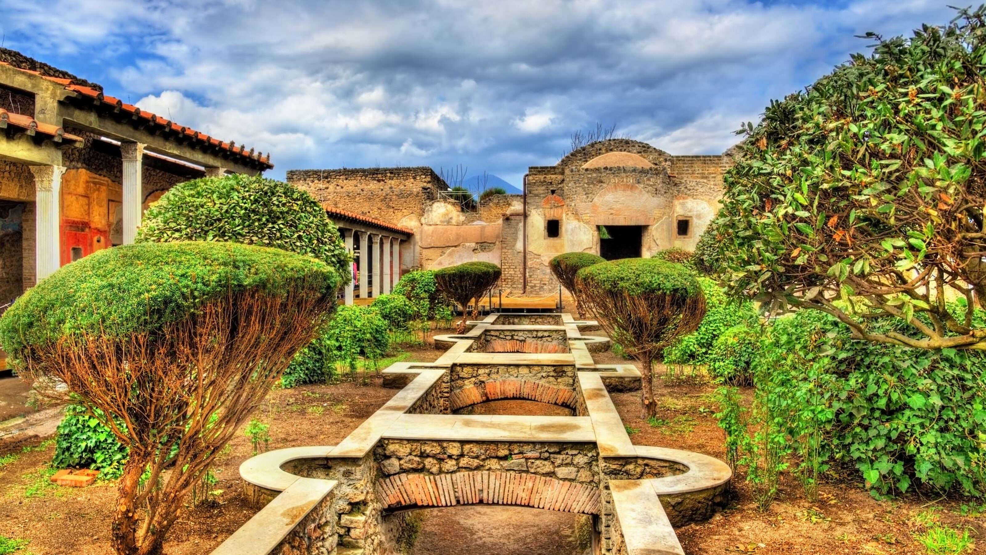 Historic stone garden structures with rectangular water channels and rounded bushes at an archaeological site.