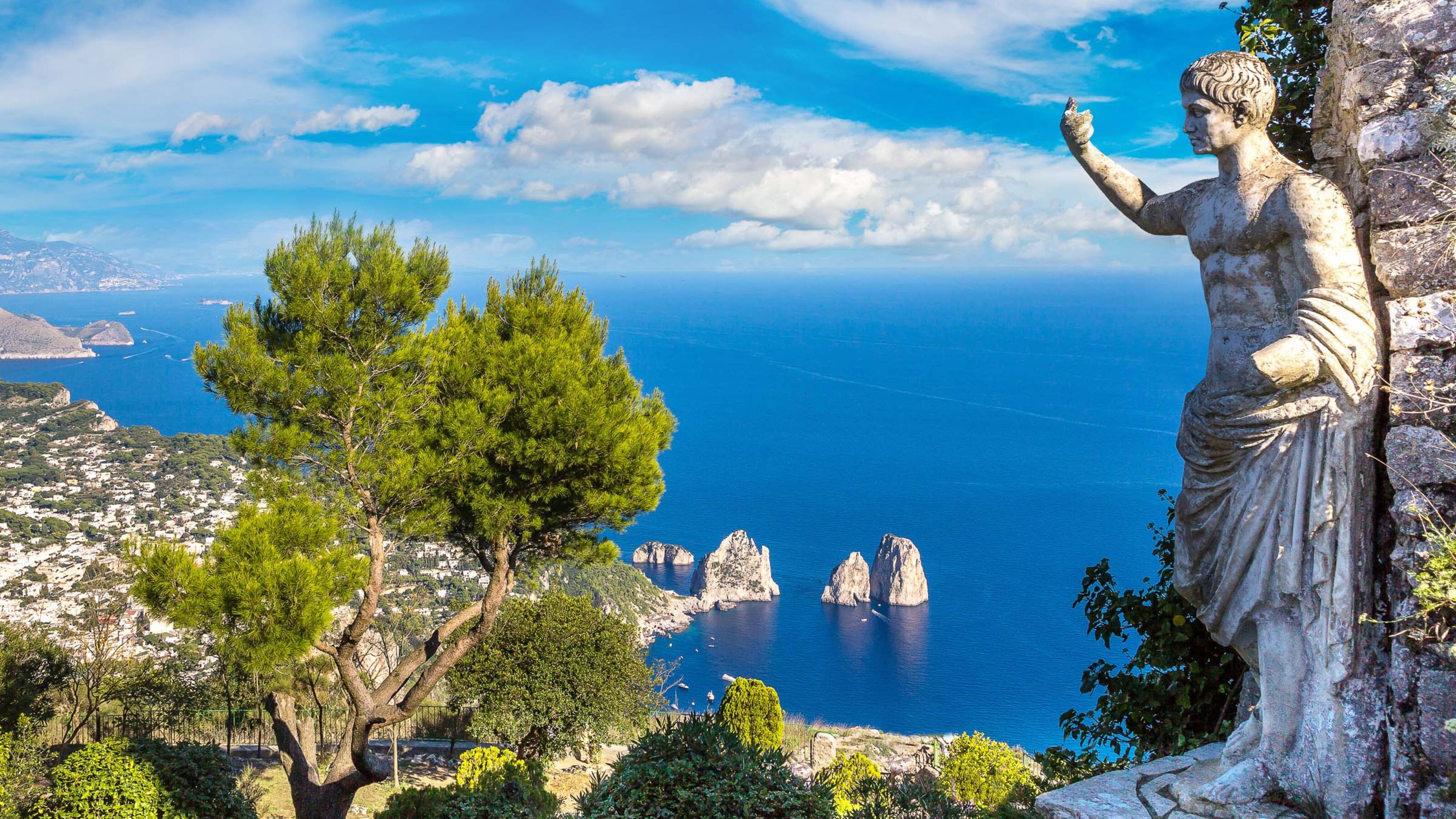Stone statue of a Roman emperor overlooking a high coastal view of the sea and iconic rock stacks in Capri.