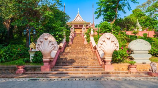 A wide staircase featuring large white Naga snake statues leading up to a traditional temple on a hill.