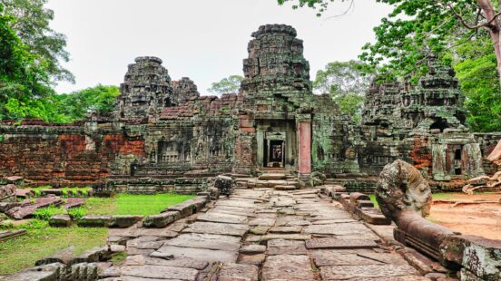 A wide stone path leading into an ancient temple complex with weathered stone towers and green vegetation.