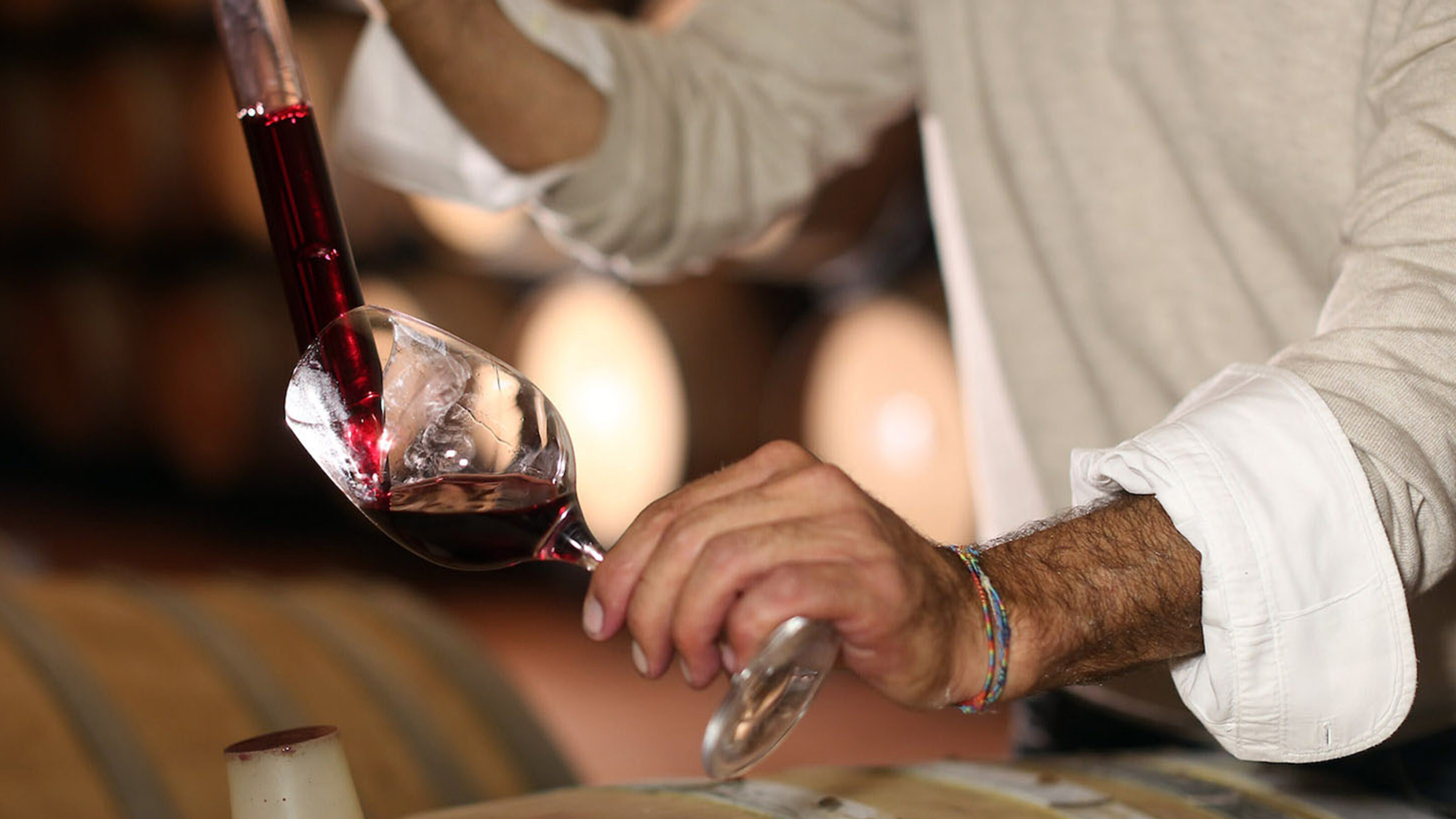 Close-up of red wine being poured from a glass tube into a wine glass in a cellar.
