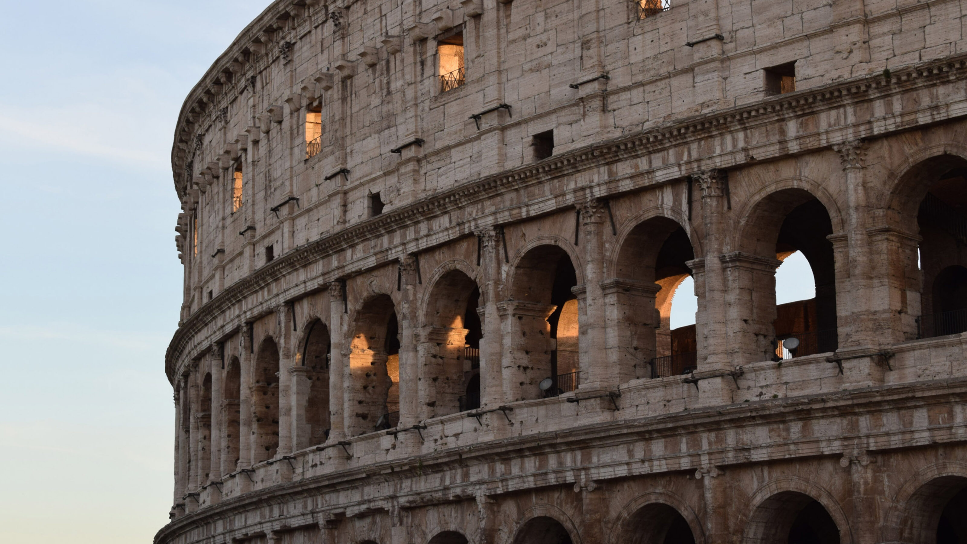 Detail of the Colosseum arches with warm light glowing from within at dusk.