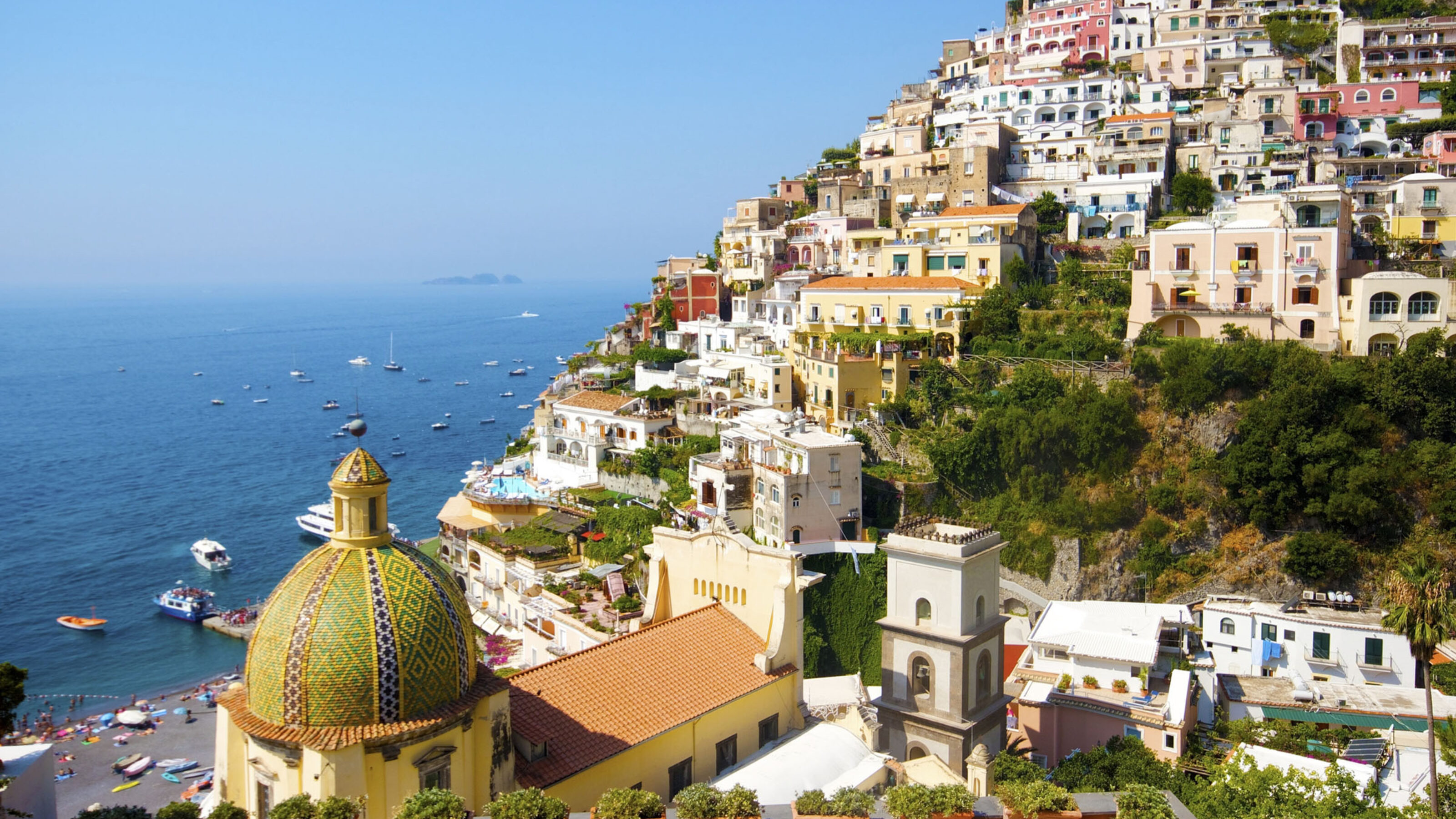 Hillside view of colorful coastal buildings and a yellow domed church overlooking the ocean.