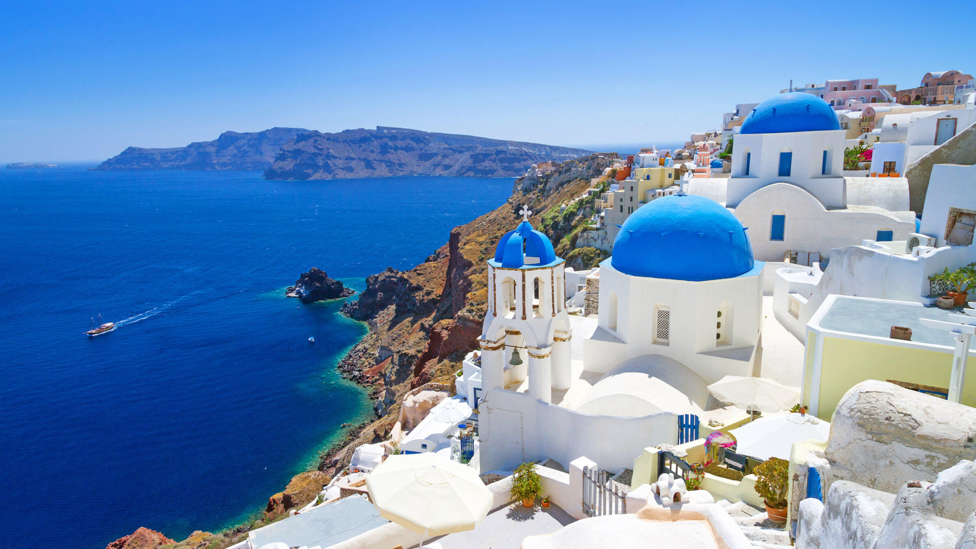 White buildings with bright blue domes on a cliffside overlooking the Aegean Sea in Santorini, Greece.