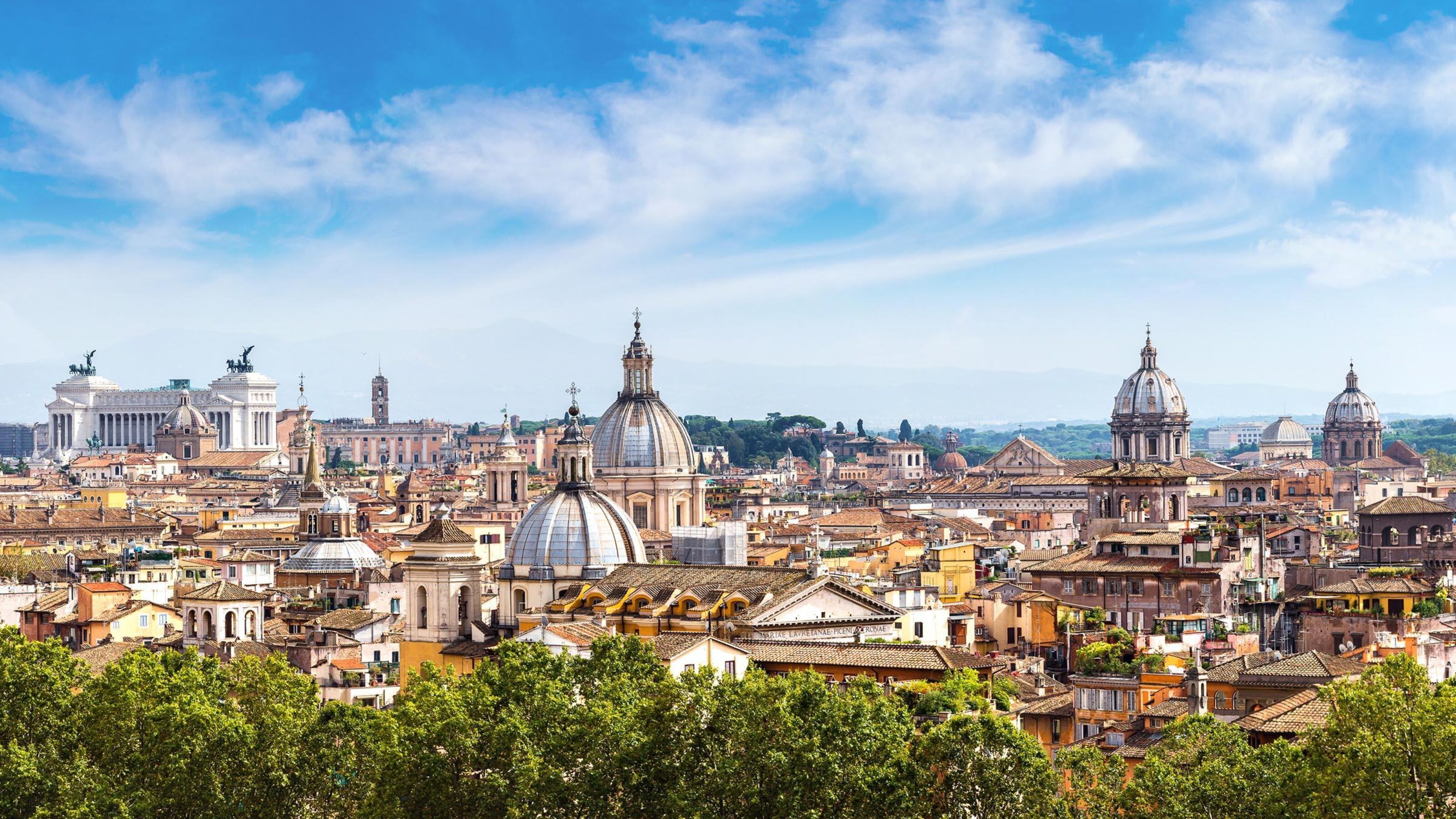 Panoramic view of the Rome skyline with historic domes and stone buildings under a clear blue sky.