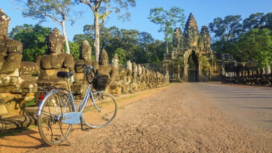 A blue bicycle parked on a path near a row of stone statues leading to an ancient carved temple gate.