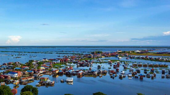 Aerial view of a village with many colorful houses built on stilts over a large body of water.