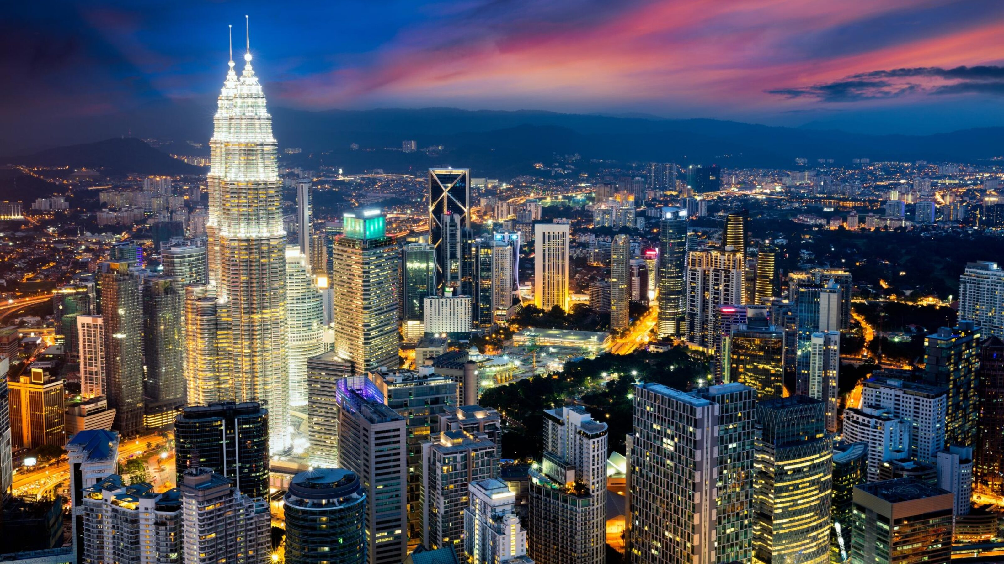 The Petronas Twin Towers stand prominently in the center of the Kuala Lumpur city skyline during the blue hour.