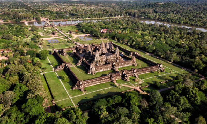 Aerial view of a large, ancient stone temple complex surrounded by lush green forests and clearings.