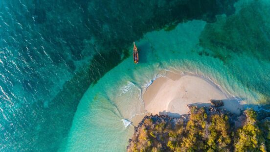Top-down view of a boat in clear blue water next to a small sandy island with green vegetation.