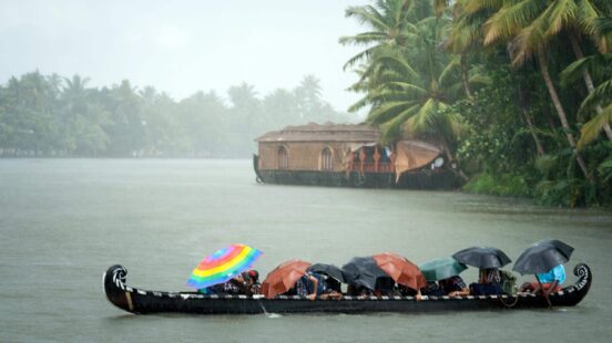 Monsoon time in Kerala, a group of people huddle under colourful umbrellas in a long canoe in a rainstorm on a Kerala river