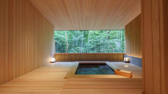 A minimalist wooden bathroom featuring a square recessed tub and a large window overlooking a bamboo grove.