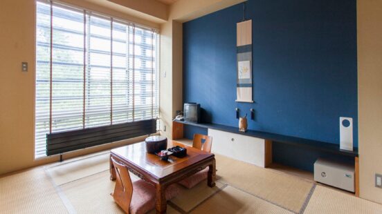 A tatami room with a low table, wooden chairs, and a striking blue accent wall featuring a hanging scroll.