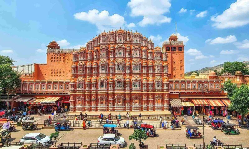 Pink sandstone windows of the Hawa Mahal rise above bustling street life in Jaipur, India.