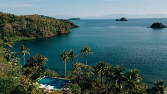 Elevated view of a private infinity pool and lounge area overlooking a secluded, deep blue tropical cove and islands.