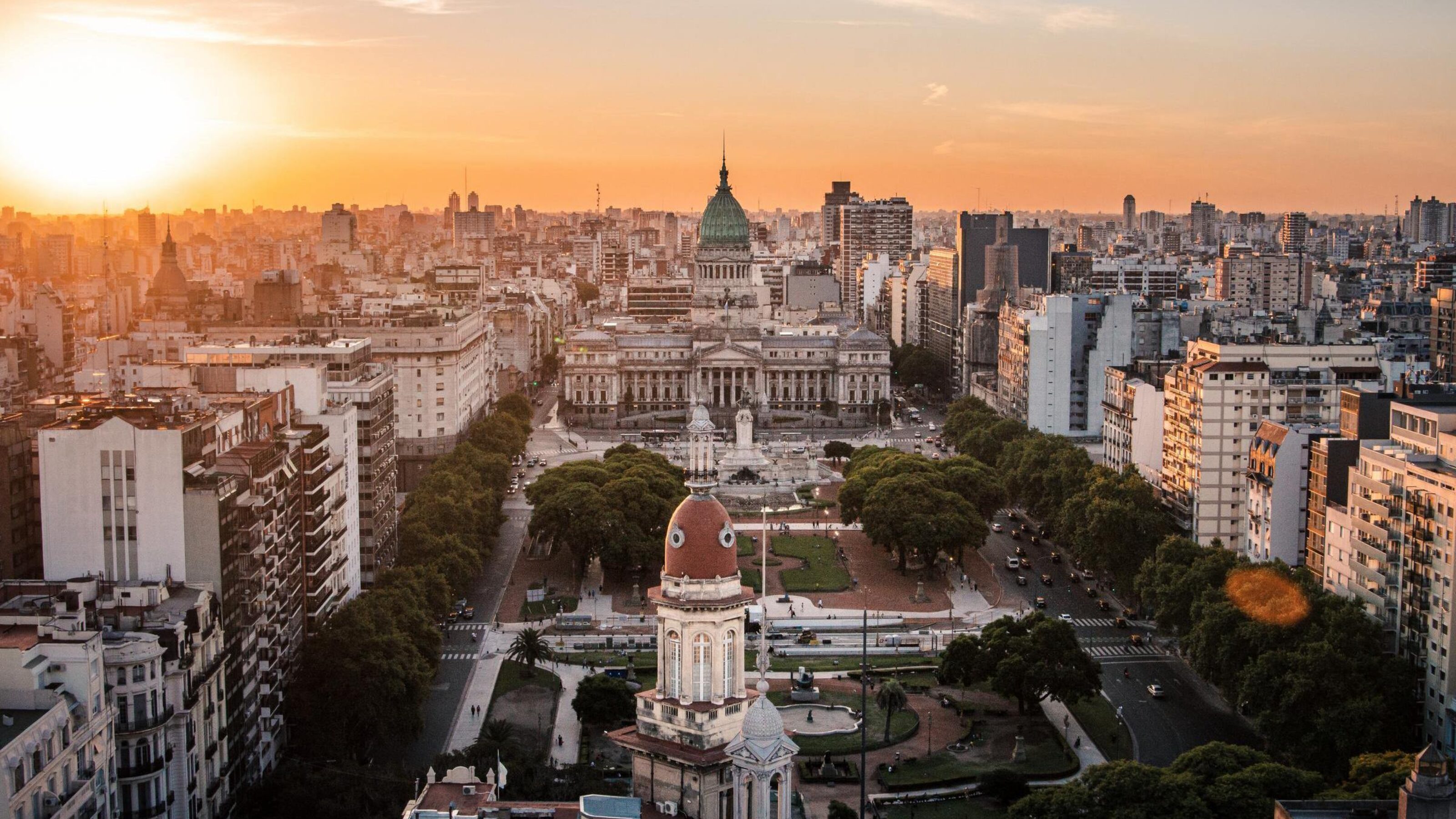 High-angle view of a large city plaza leading to a domed government building under a bright sunset sky.