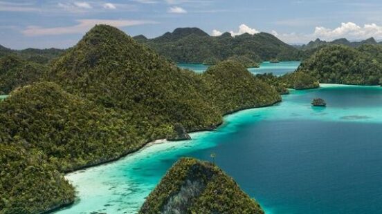 High angle view of lush green tropical islands surrounded by crystal clear turquoise water and sandy reefs.