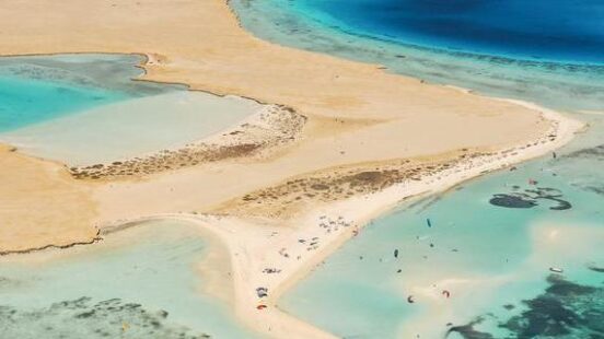 High-angle aerial view of a white sandbar and desert coastline meeting clear turquoise and deep blue ocean waters.