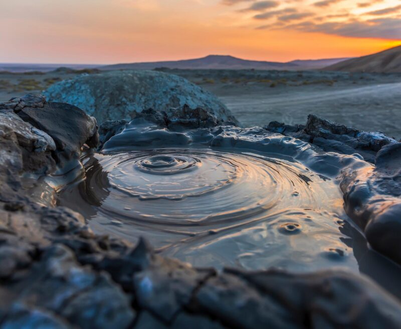 Mud bubbles to the surface of a mud volcano pool in Gobustan, Azerbaijan, set against a warm sunset.