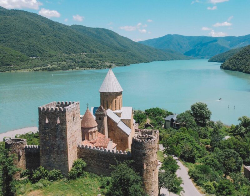 Stone towers of Ananuri Fortress overlook turquoise waters in Georgia.