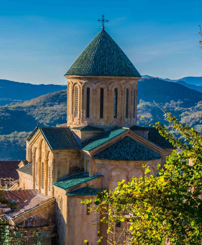 The green-tiled dome of Gelati Monastery stands against forested hills in Kutaisi, Georgia.