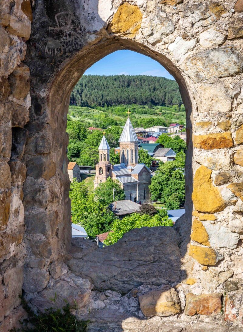 A stone archway frames the spires of Surp Gevork Church amongst Surami’s green hills in Georgia.