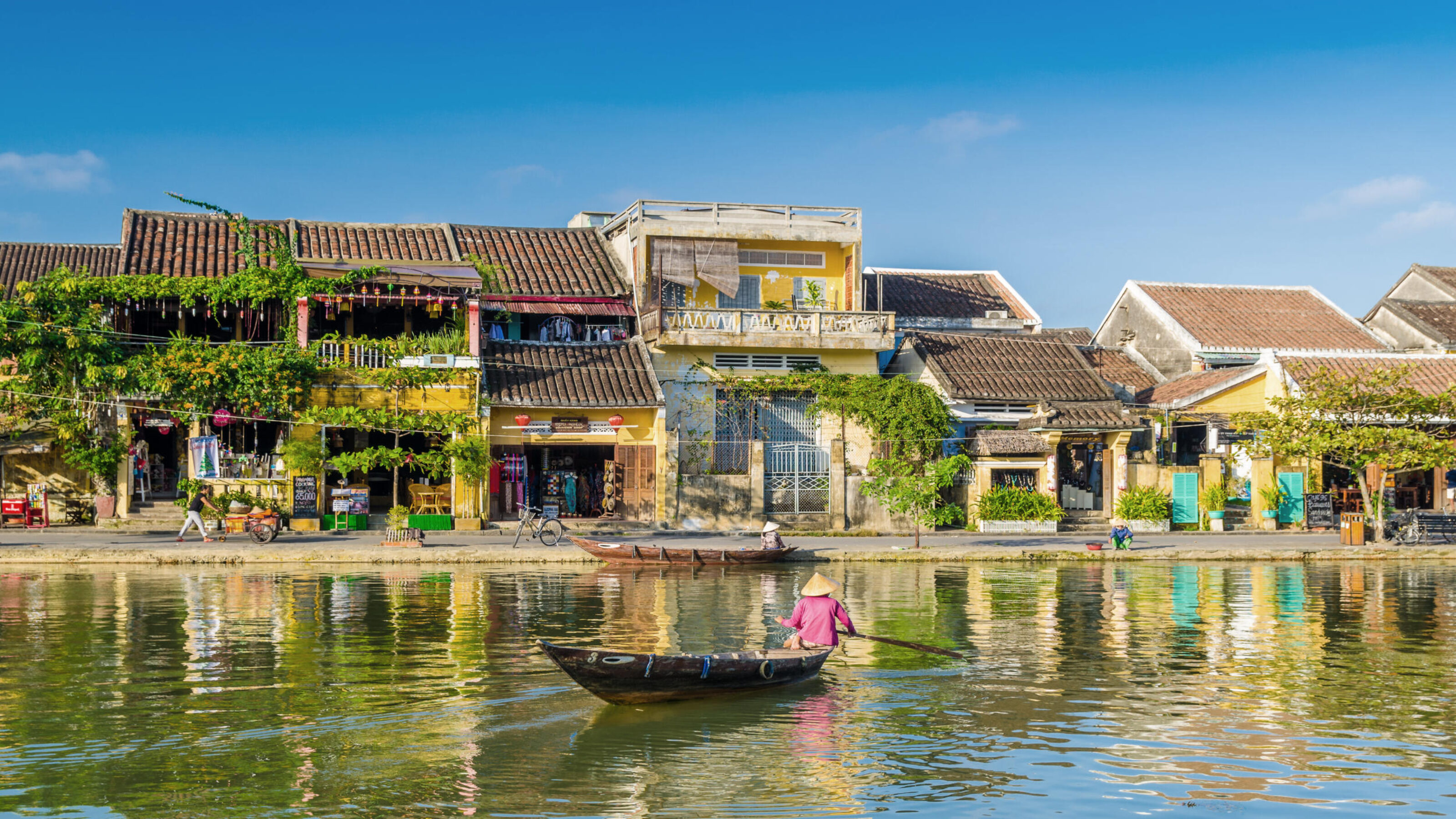 A person in a boat on a river reflecting the yellow historic buildings of an ancient waterfront town.