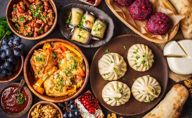 Traditional Georgian cuisine background. Khinkali, phali, chahokhbili, lobio, cheese, eggplant rolls on dark background, top view.