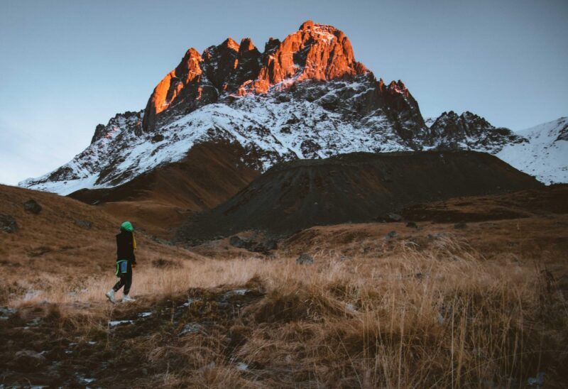Female hiker hike trekking in beautiful Juta valley hiking route with scenic mountain snowy peak background. Kazbegi national park landscape