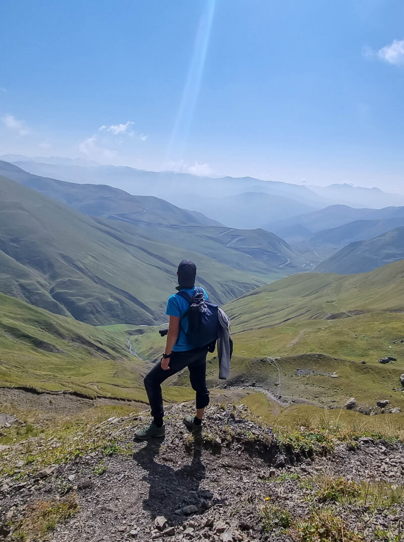 A man watching the sharp mountain peaks of the Chaukhi massif form the Chaukhi Pass in the Greater Caucasus Mountain Range in Georgia, Kazbegi Region. The female backpacker enjoys the calmness. Hike