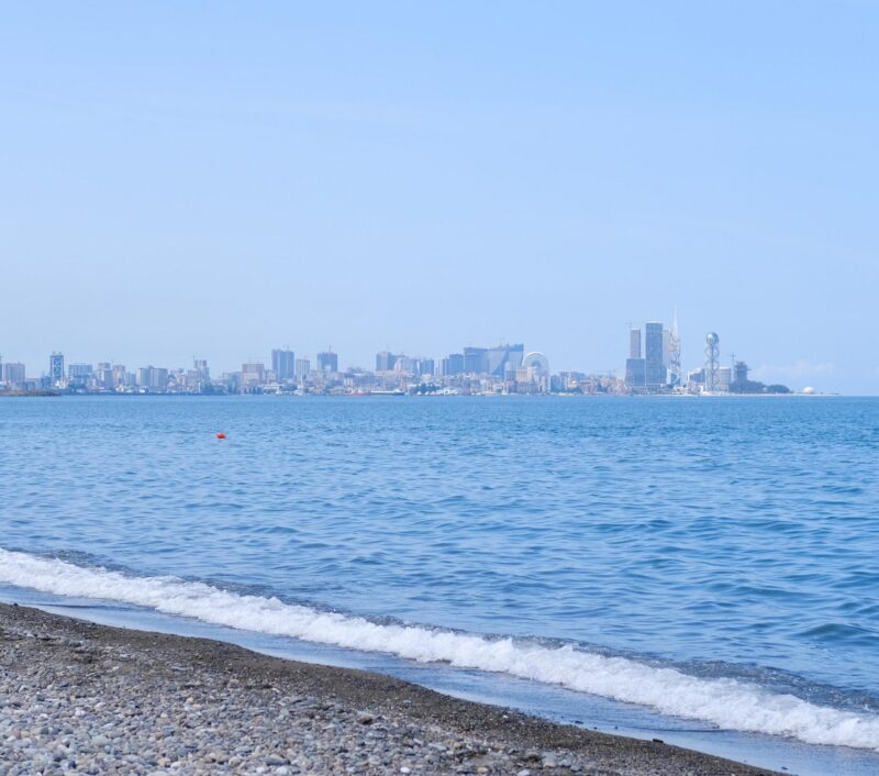 Batumi, Georgia – June 11, 2023. Pebble coast of the Black Sea. The water and sky are blue, sunny day. Tourism and beach holiday concept. Panoramic advertising banner with space for text