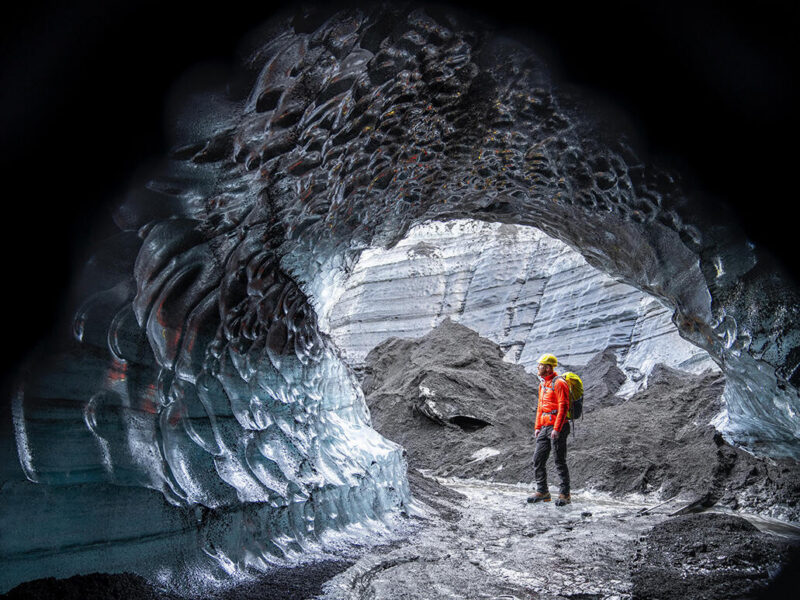 Hiker standing by ice cave at glacier in Iceland