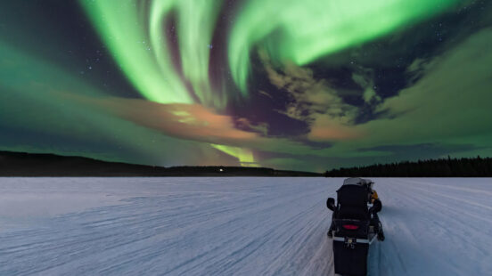 Vibrant green aurora borealis dancing in the sky over a snow-covered landscape with a snowmobile.