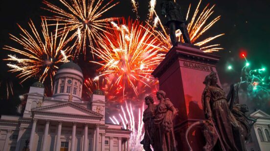 Bright fireworks exploding over a white domed cathedral and a bronze statue at night.