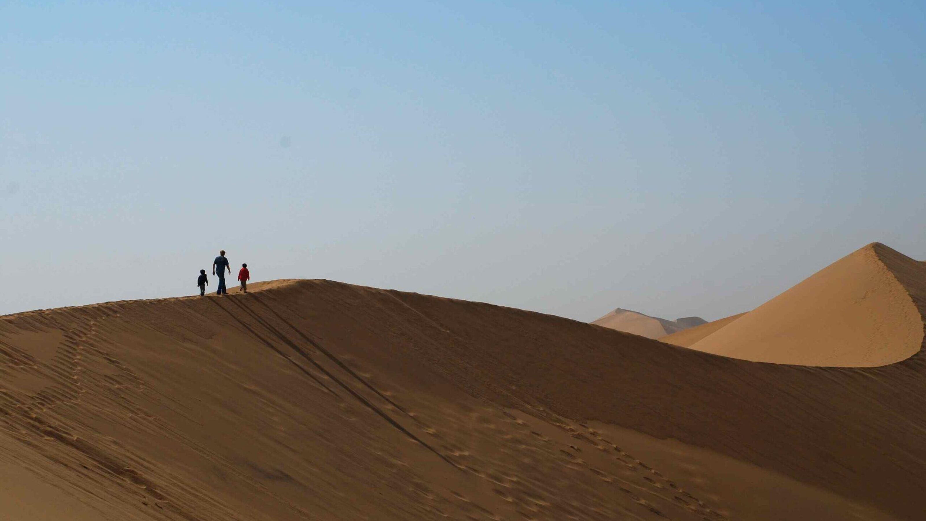 Silhouette of three figures walking on the crest of a high sand dune in the desert.