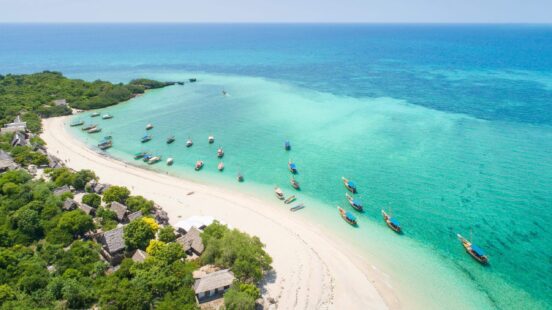 The curved coast of beautiful white sand beach with boats moored in the crystal azure waters of Zanzibar Island, Tanzania.