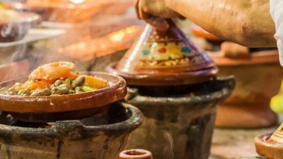 Close-up of several decorative ceramic tagines cooking over heat with steam rising from the food.