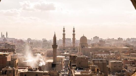 A cityscape of Cairo with mosque minarets seen through a circular stone archway during the day.