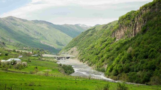 A scenic view of a lush green mountain valley with a winding river and steep, tree-covered cliffs.