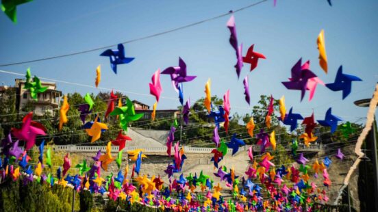 Many colorful paper pinwheels hanging from wires against a clear blue sky.