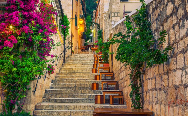 Cozy narrow street with street cafe and restaurant at morning. Rustic street with stone houses and colorful bougainvillea mediterranean flowers, Hvar town, Hvar island, Dalmatia, Croatia, Europe