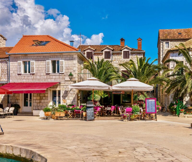 A colorful panorama of a Mediterranean resort town in summer, with restaurants and cafes along the waterfront promenade. Stari Grad, Hvar Island, Croatia.