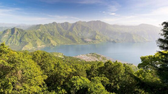 High angle view of a blue lake surrounded by green mountains and a small coastal town.