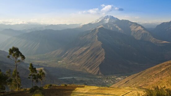Panoramic view of a sunlit mountain valley with a village and terraced fields.