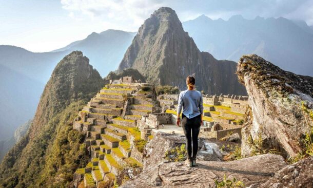 A person looking out over the historic ruins of Machu Picchu surrounded by steep green mountains.