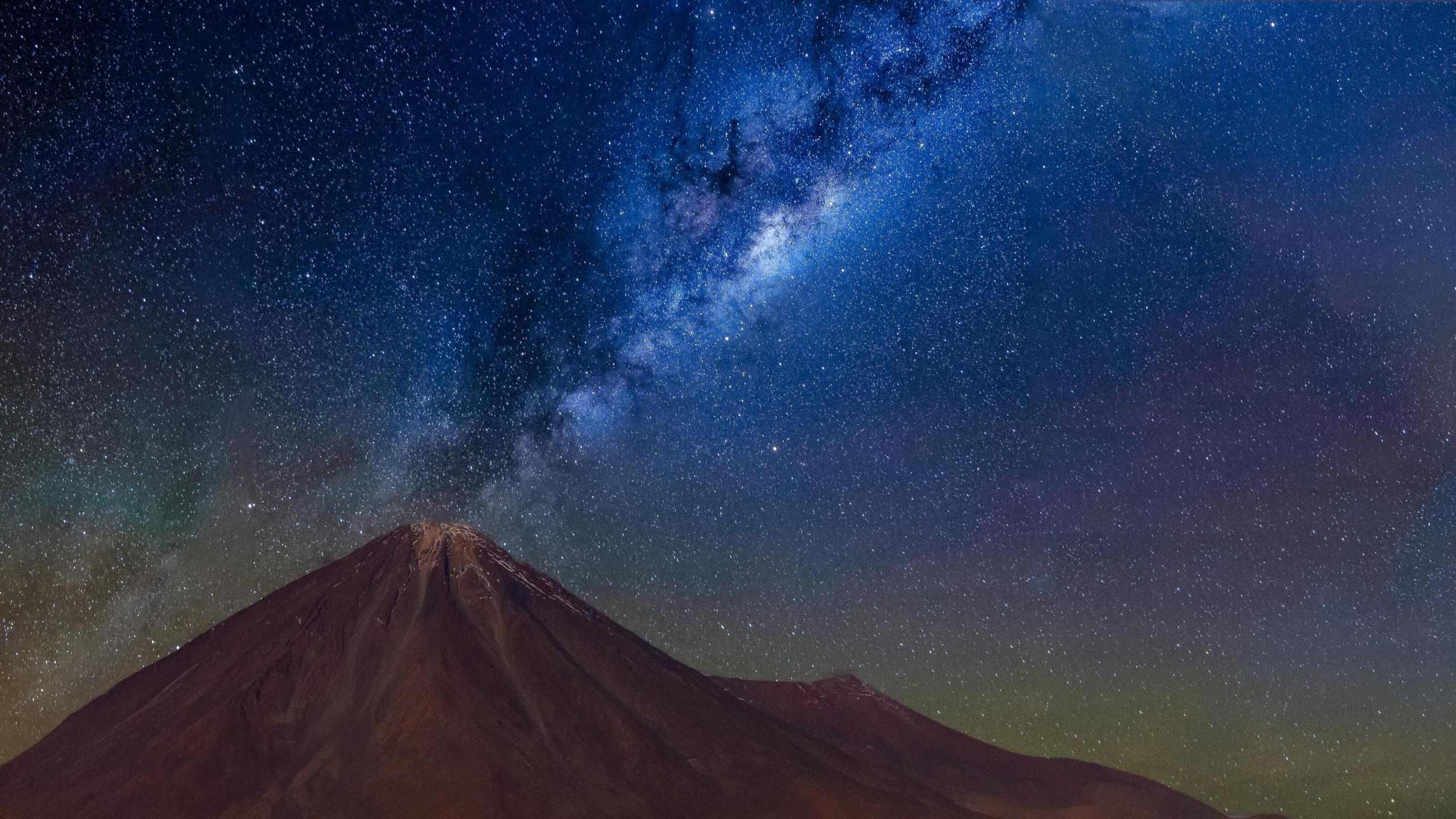 A clear night sky filled with stars and the Milky Way galaxy over a silhouette of a mountain.