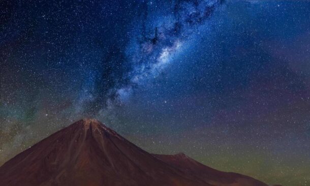 A clear night sky filled with stars and the Milky Way galaxy over a silhouette of a mountain.