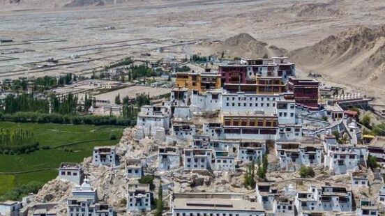 A large Buddhist monastery built onto a rocky hillside in a vast, arid mountain valley.