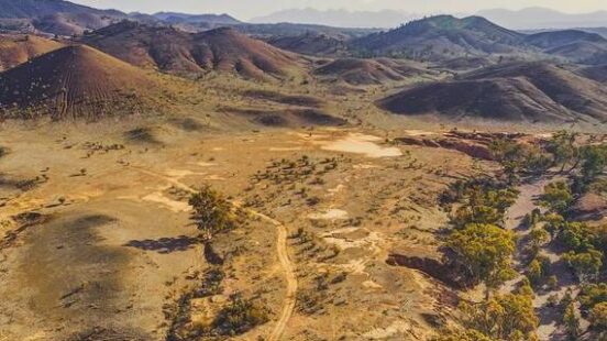 Aerial view of a dirt road winding through dry, rolling hills and sparse vegetation.
